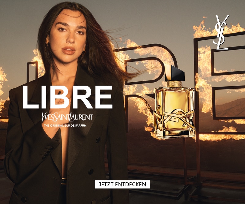 Yves Saint Laurent Libre Eau de Parfum – Flakon vor brennenden LIBRE-Buchstaben mit Dua Lipa im schwarzen Blazer
